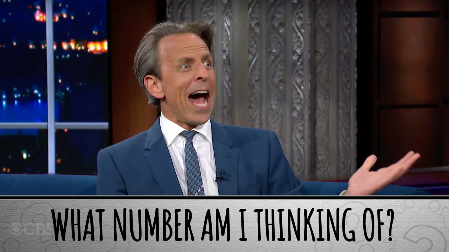 A man in a suit gestures on a talk show with his mouth open. The caption at the bottom reads, "What number am I thinking of?"