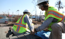 Two people in hard hats and high-visibility vests work on a roof.