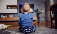 A young child watches a TV screen.