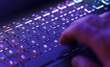 A person working on a neon computer keyboard with colorful backlighting.