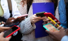 A group of young people stand huddled in a circle using smartphones. 