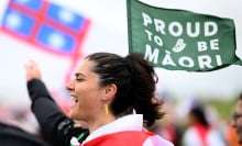 A person cheers and holds up a green flag that reads "Proud to be Maori."