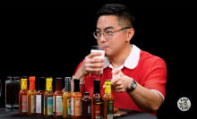 A man sits at a table covered in sauce bottles, sipping a glass of milk.