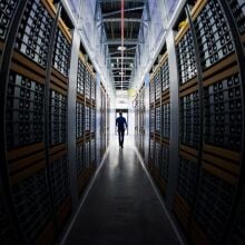 A man in silhouette, walking through racks of computers in a data center.