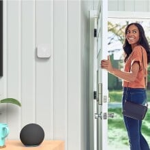 a person leaves the front door of a house, while looking back inside and smiling. On the wall is an amazon smart thermostat