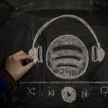 A person drawsingthe Spotify logo wearing a pair headphones in chalk. 