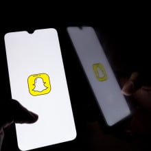 A hand holds a glowing phone showing the Snapchat logo in a dark room.