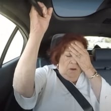 A woman sitting in the back seat of a car covers her face with one hand.