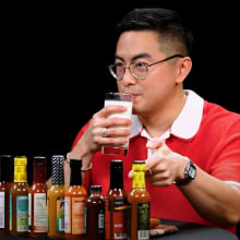 A man sits at a table covered in sauce bottles, sipping a glass of milk.