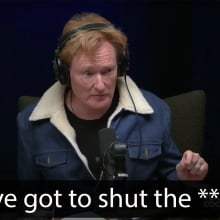 A man sits at a table in a dark podcast studio.