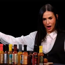 A woman throws her arms wide while sitting in front of a table covered in sauce bottles.