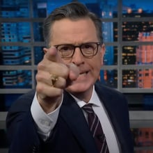 A man in a suit point angrily at the camera on a talk show stage.