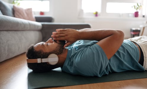 A man laying on the floor in a relaxed pose listening to headphones. 