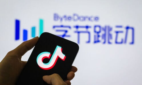 A person holds a smartphone displaying the Douyin logo (the Chinese version of TikTok), with the ByteDance company logo in the background