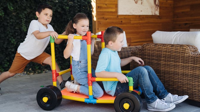 Three kids playing with the Omagles builder set outdoors.