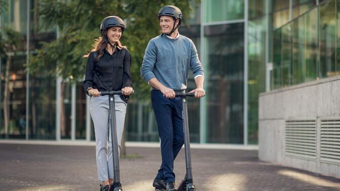 Two people riding the Segway Ninebot KickScooter ES2 with helmets on.