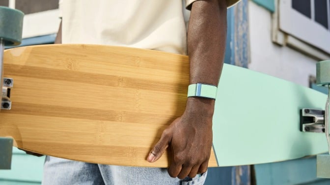 a person wears a light turquoise whoop band on their wrist while holding a wooden longboard that matched the color of the whoop band