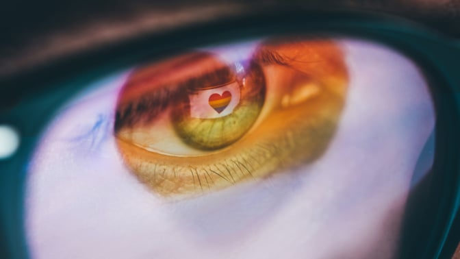 Woman with a rainbow heart reflected in her eyes and glasses.