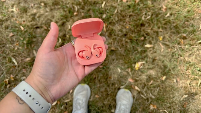 A person holding a pair of Beats Fit Pro against a lawn