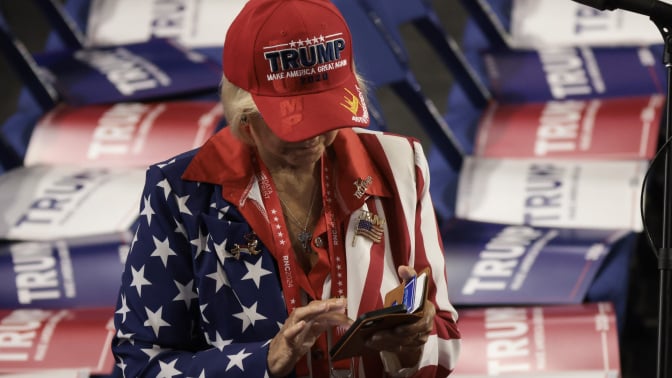 a woman in a trump hat scrolling on her phone, surrounded by trump signs