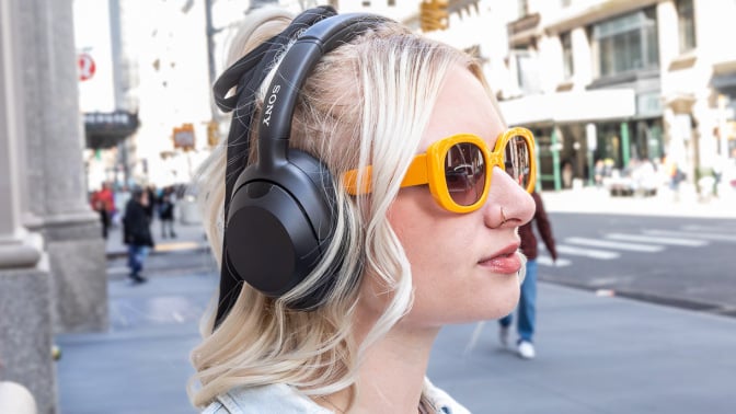 hip young woman in yellow sunglasses wearing Sony headphones on city street