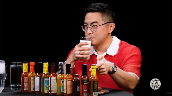 A man sits at a table covered in sauce bottles, sipping a glass of milk.