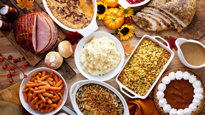 a thanksgiving table spread. there's turkey, ham, mashed potatoes, stuffing. rolls, green bean casserole, cranberry sauce