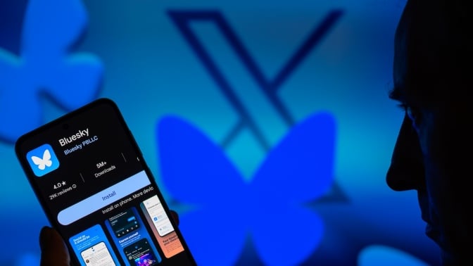 Bluesky's butterfly logo covers an X while a man looks at the Bluesky app on his phone