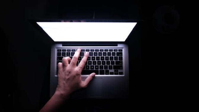 A hand hovers ominously over a keyboard against a dark background. 