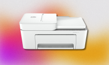 A white HP DeskJet 4255e all-in-one printer with the paper tray extended and a sheet of paper feeding into the top. It's set against a colorful, abstract background with pink, orange, and yellow tones.