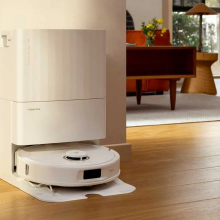 White Roborock vacuum and dock sitting against wall with living room furniture in background