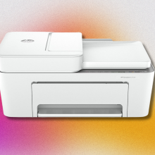 A white HP DeskJet 4255e all-in-one printer with the paper tray extended and a sheet of paper feeding into the top. It's set against a colorful, abstract background with pink, orange, and yellow tones.