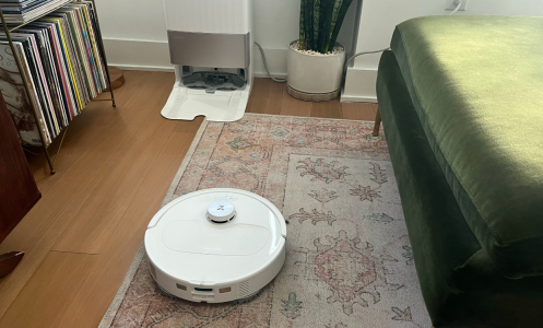 Roborock Qrevo Master robot vacuum cleaning rug with self-empty dock, record organizer, and green couch in peripherals