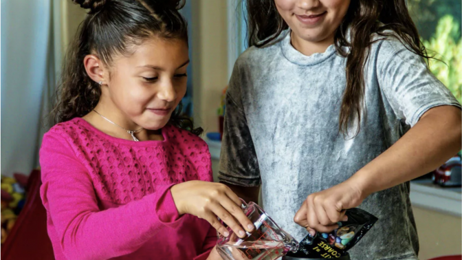 Two girls holding component parts of the Nat Geo Rock Tumbler kit while following the kit's instructions