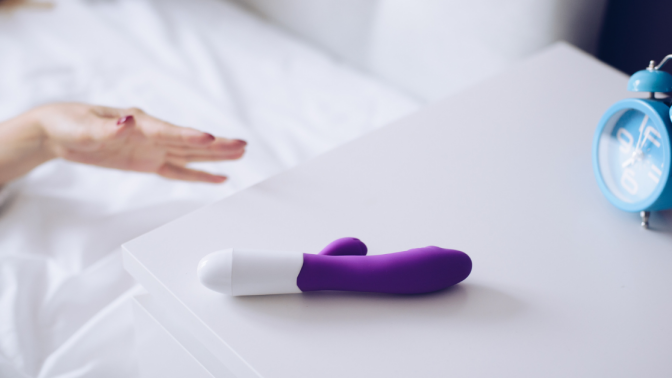 Young woman holding sex toy dildo vibrator in bed