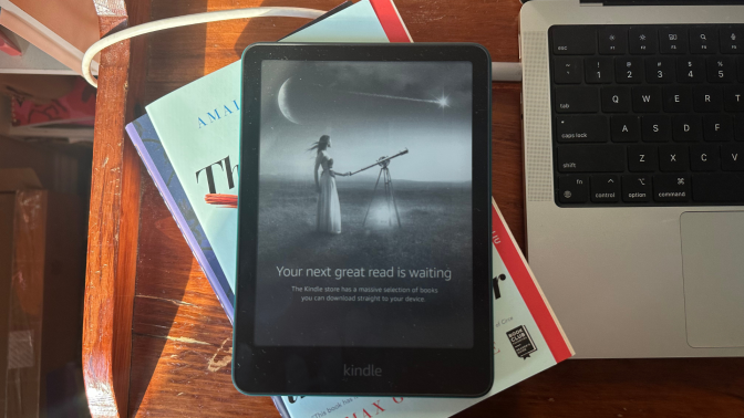 A Kindle Paperwhite on top of a stack of books.