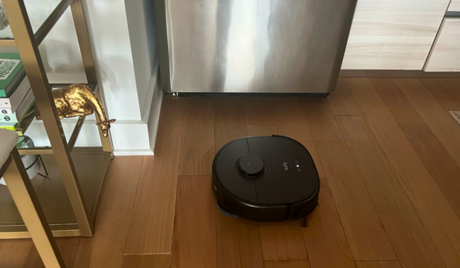 Eufy robot vacuum cleaning hardwood with refrigerator, bar stool, and cabinets in peripherals